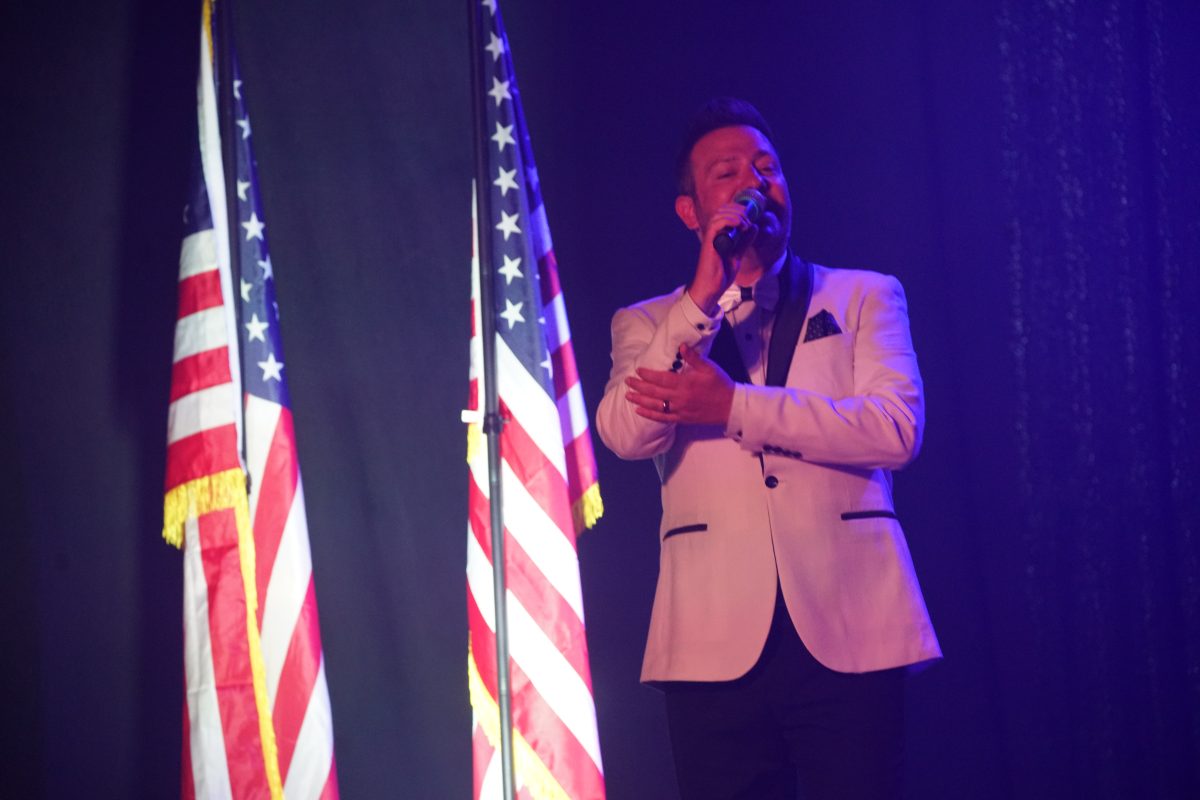 America - The Show singer in a white dinner jacket between American flags, Las Vegas
