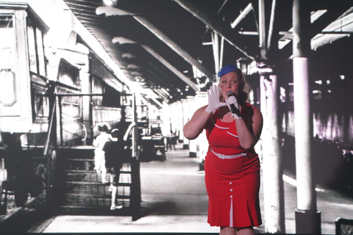 America - The Show singer in a red 1940s dress on a vintage train platform backdrop, Las Vegas